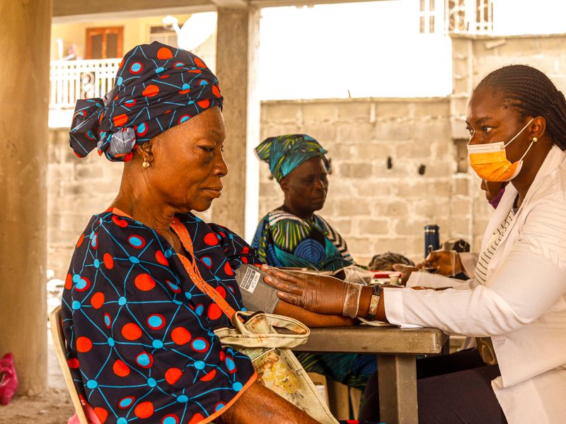 A health worker checks an older woman&rsquo;s blood pressure as she sits comfortably.