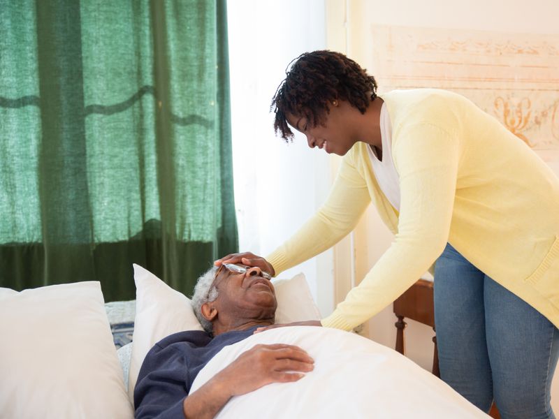 A carer gently tending to an older woman's hands while she sits comfortably at home.